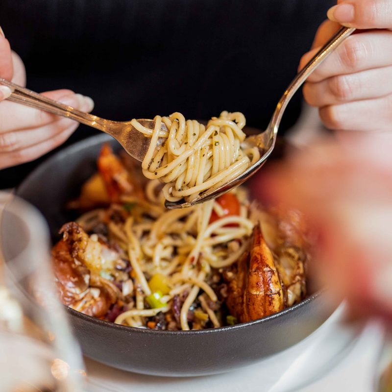 Person isst Spaghetti mit Garnelen aus einer Schüssel.