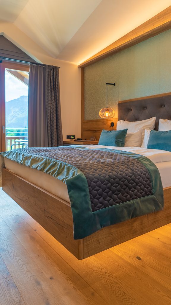 Hotelzimmer mit Doppelbett, Holzdesign und Balkontür mit Bergblick.