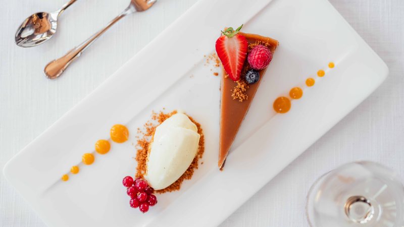 Stück Schokoladentarte mit Vanilleeis und frischen Beeren auf einem weißen Teller.