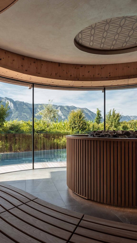 Wellness-Ruheraum mit Holzverkleidung, Panoramafenster und Blick auf Pool und Berge.