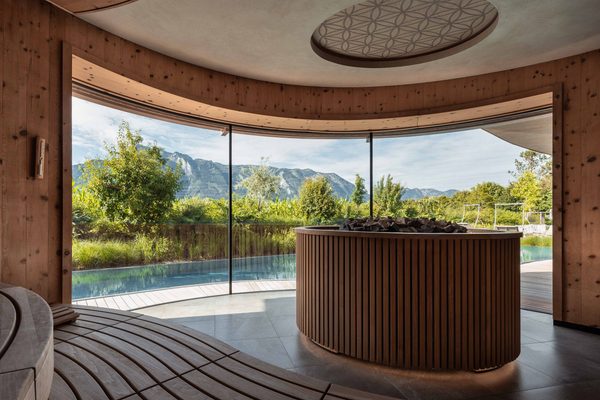 Wellness-Ruheraum mit Holzverkleidung, Panoramafenster und Blick auf Pool und Berge.